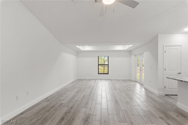 empty room featuring ceiling fan, a skylight, a raised ceiling, and light hardwood / wood-style flooring