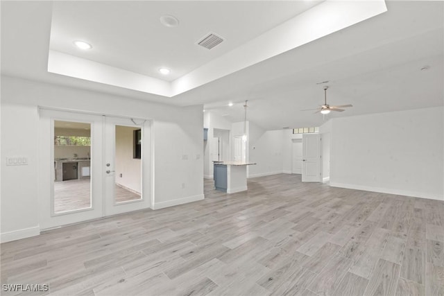 unfurnished living room with a tray ceiling, french doors, ceiling fan, and light wood-type flooring