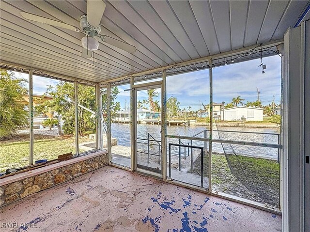 unfurnished sunroom featuring ceiling fan and a water view