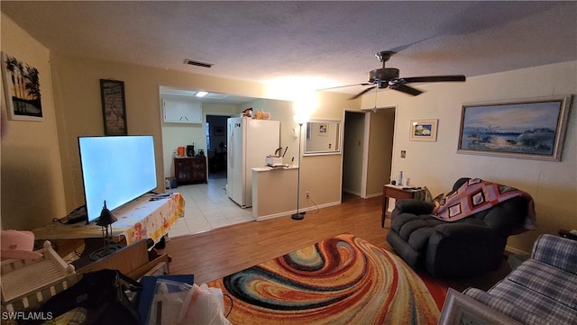 living room with light wood-style floors, visible vents, ceiling fan, and a textured ceiling