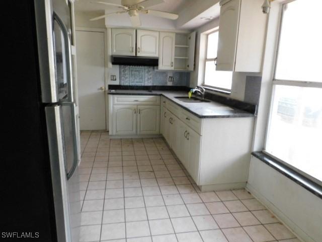 kitchen featuring ceiling fan, sink, light tile patterned floors, and stainless steel refrigerator