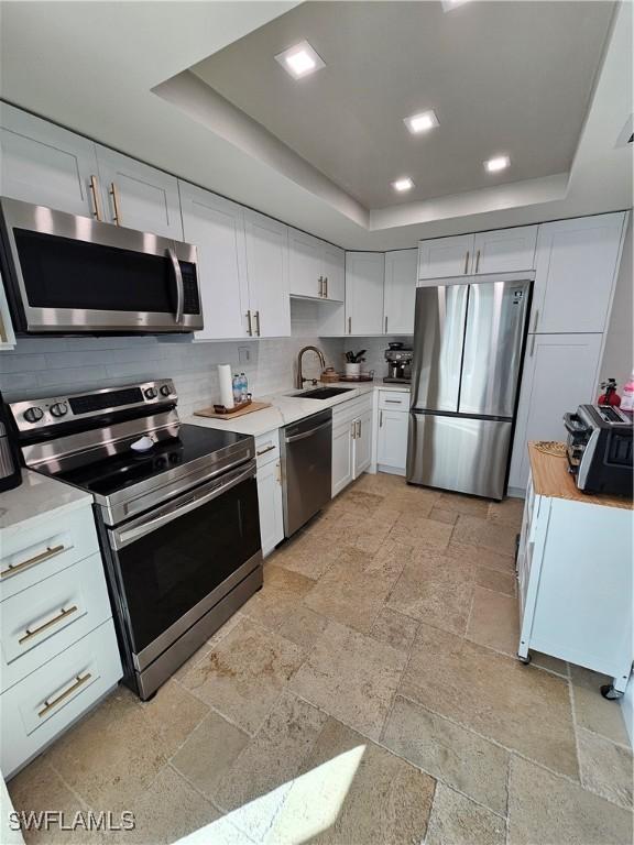 kitchen featuring white cabinetry, appliances with stainless steel finishes, a raised ceiling, and sink