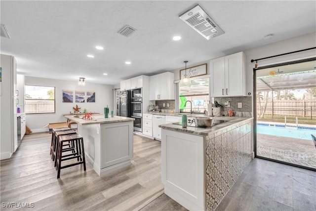 kitchen with a breakfast bar, white cabinetry, light hardwood / wood-style floors, a kitchen island, and decorative light fixtures