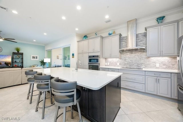 kitchen with a kitchen island with sink, wall chimney range hood, gray cabinetry, and sink