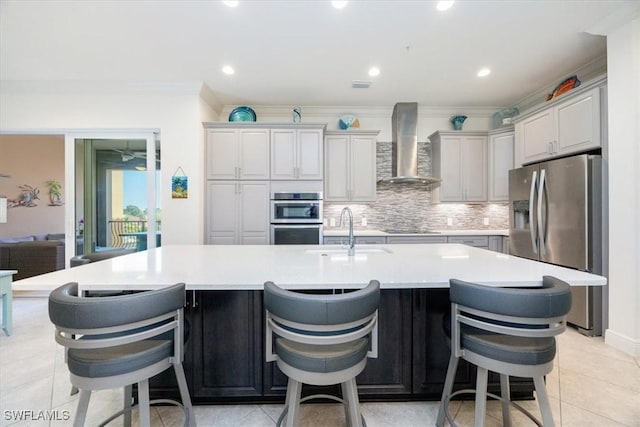 kitchen with wall chimney range hood, sink, a breakfast bar area, stainless steel appliances, and a large island with sink