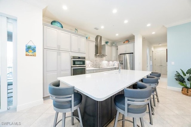 kitchen featuring sink, a kitchen bar, wall chimney exhaust hood, stainless steel appliances, and a spacious island