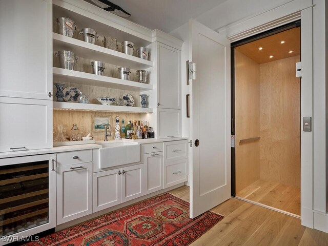 bar with wine cooler, a dry bar, light wood-style floors, elevator, and a sink