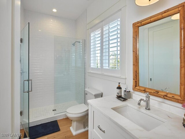 bathroom featuring toilet, wood finished floors, vanity, a shower stall, and recessed lighting