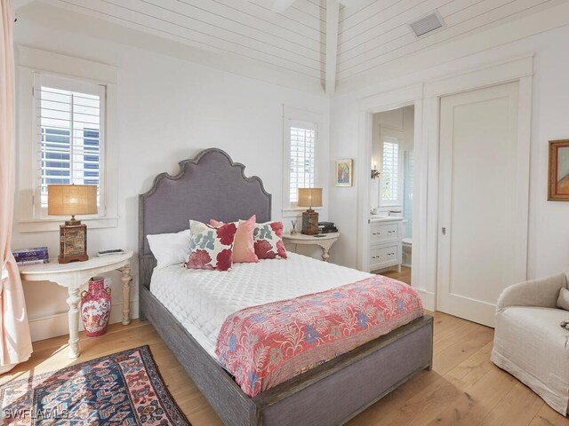 bedroom featuring ensuite bathroom, multiple windows, visible vents, and light wood-style floors