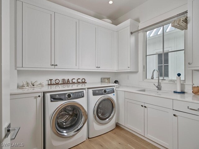 washroom with cabinet space, light wood-style floors, separate washer and dryer, and a sink