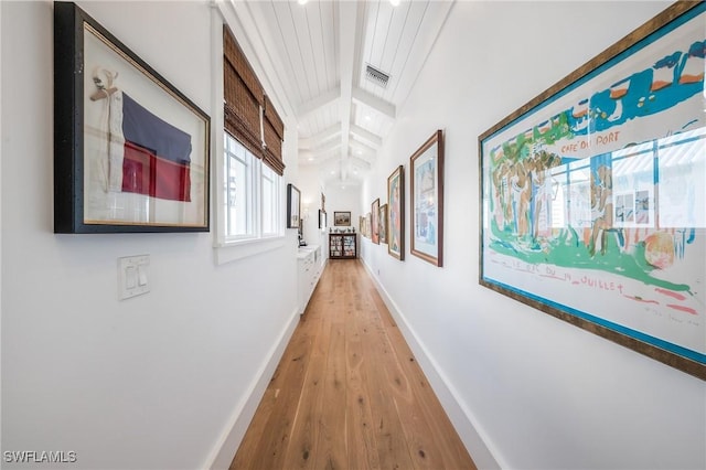 corridor featuring light wood-type flooring, visible vents, baseboards, and beam ceiling