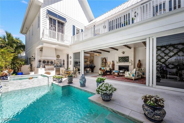 rear view of property with an outdoor kitchen, a balcony, an in ground hot tub, an outdoor pool, and a patio area