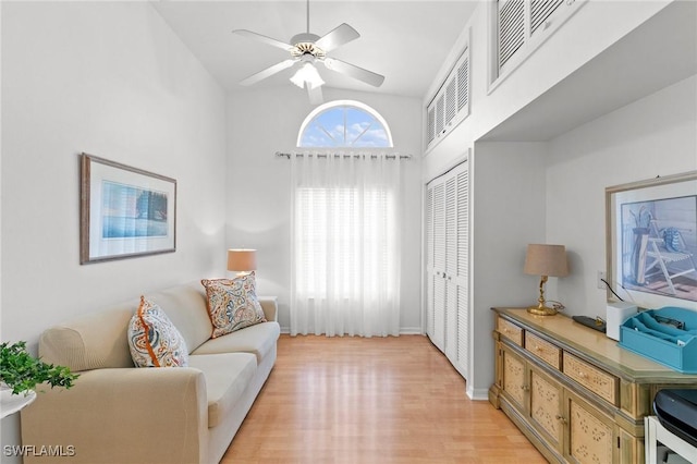 living area with ceiling fan, light hardwood / wood-style floors, and a high ceiling