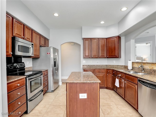 kitchen with light stone counters, stainless steel appliances, sink, and a kitchen island