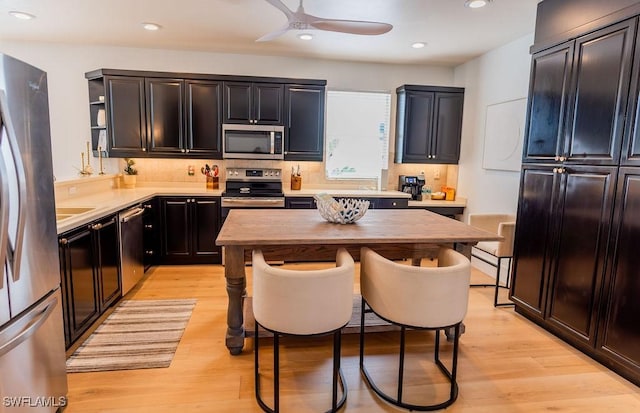 kitchen with backsplash, ceiling fan, appliances with stainless steel finishes, and light wood-type flooring