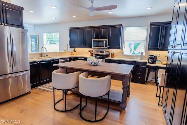 kitchen with sink, light hardwood / wood-style flooring, ceiling fan, backsplash, and stainless steel appliances