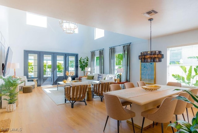 dining area featuring an inviting chandelier, light hardwood / wood-style flooring, french doors, and a high ceiling