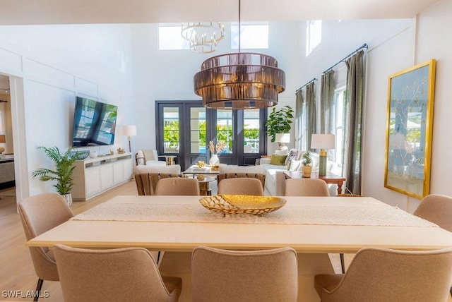 dining room featuring a notable chandelier, a towering ceiling, and light wood-type flooring