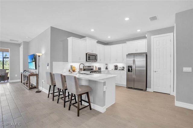 kitchen featuring sink, appliances with stainless steel finishes, white cabinetry, a kitchen breakfast bar, and kitchen peninsula