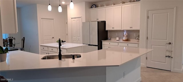 kitchen with sink, hanging light fixtures, stainless steel fridge, an island with sink, and white cabinets