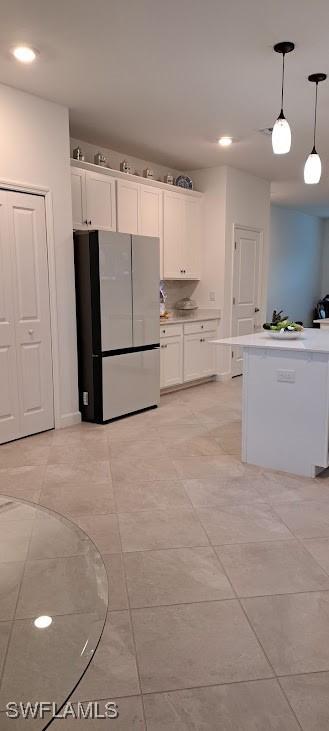 kitchen with fridge, decorative light fixtures, light tile patterned floors, and white cabinets