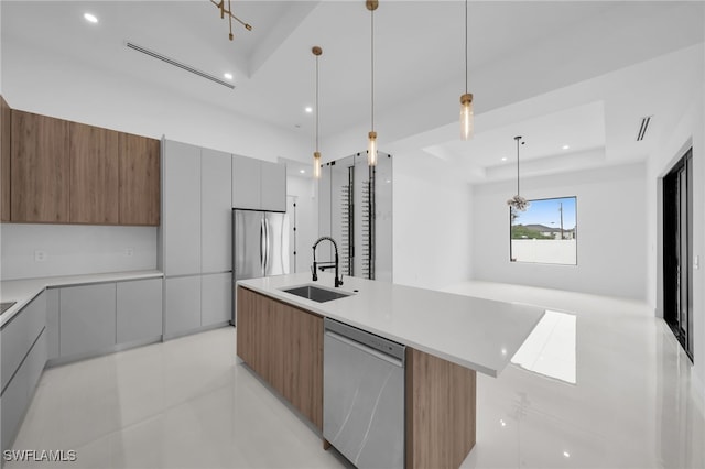 kitchen with pendant lighting, sink, appliances with stainless steel finishes, a raised ceiling, and a large island with sink