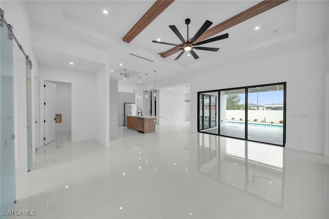 unfurnished living room with ceiling fan, sink, a barn door, and beamed ceiling