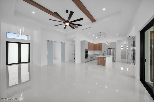 kitchen with stainless steel fridge, hanging light fixtures, a center island with sink, french doors, and a barn door