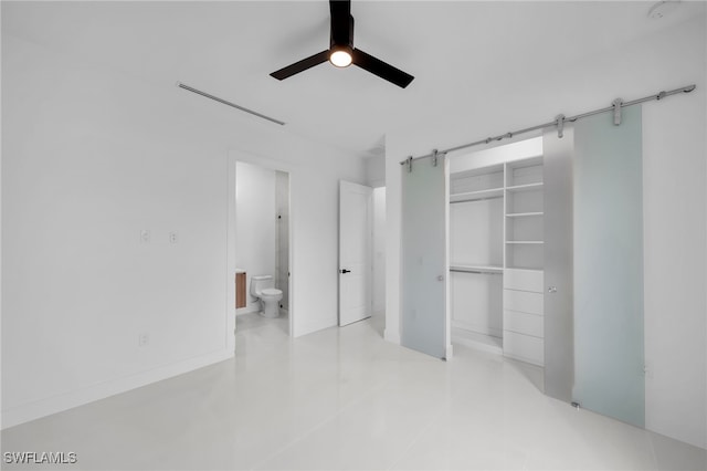 unfurnished bedroom featuring a closet, ensuite bath, a barn door, and ceiling fan