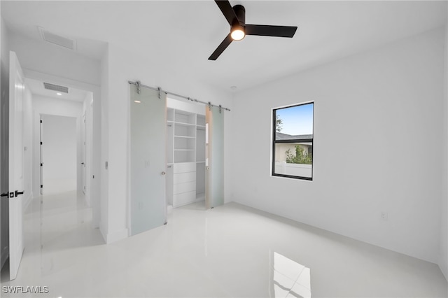 interior space featuring a walk in closet, a closet, ceiling fan, and a barn door