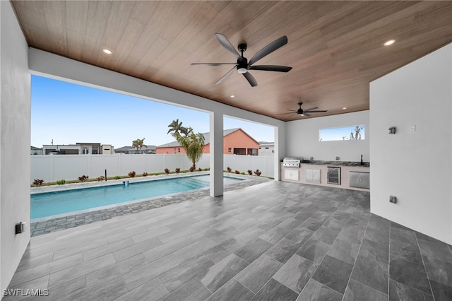 view of swimming pool featuring a patio area, grilling area, ceiling fan, and an outdoor kitchen