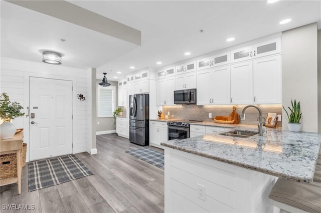 kitchen with sink, light stone counters, appliances with stainless steel finishes, kitchen peninsula, and white cabinets