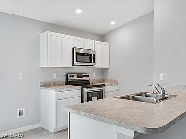 kitchen with a breakfast bar, sink, white cabinetry, appliances with stainless steel finishes, and kitchen peninsula