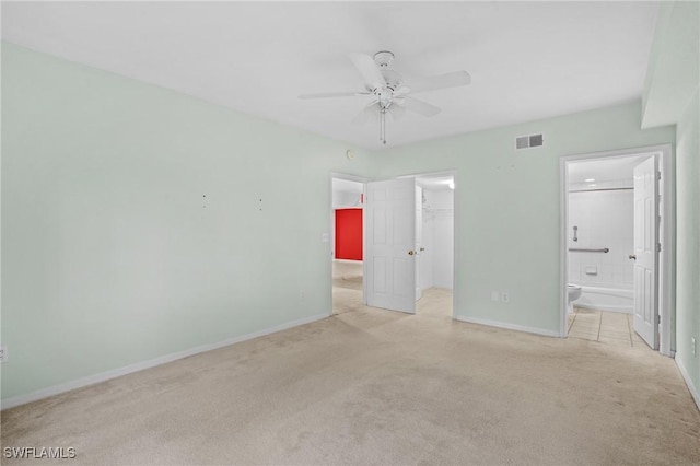 unfurnished bedroom featuring ensuite bath, a walk in closet, light colored carpet, a closet, and ceiling fan