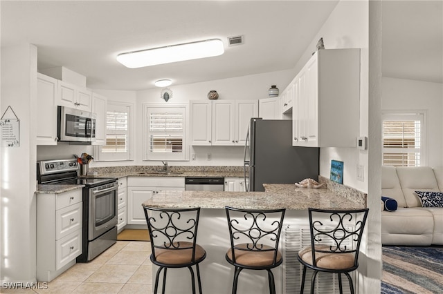 kitchen with appliances with stainless steel finishes, sink, white cabinets, a kitchen bar, and kitchen peninsula