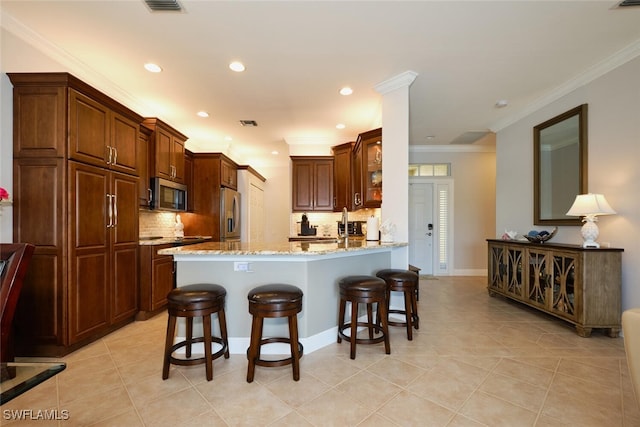 kitchen with appliances with stainless steel finishes, a kitchen breakfast bar, light stone counters, light tile patterned flooring, and kitchen peninsula