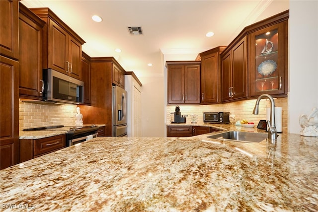 kitchen featuring stainless steel appliances, sink, light stone counters, and decorative backsplash