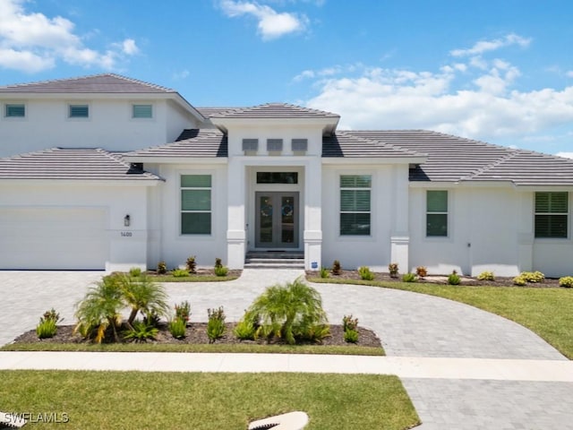 prairie-style house with a garage, a front lawn, decorative driveway, and french doors