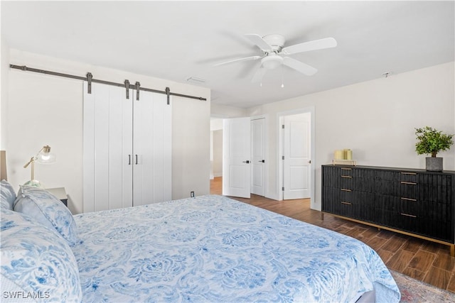 bedroom with ceiling fan, a barn door, and dark hardwood / wood-style flooring