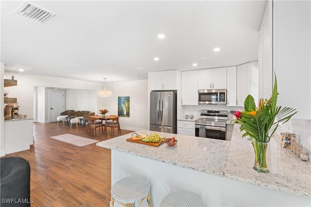 kitchen featuring white cabinets, light stone counters, kitchen peninsula, stainless steel appliances, and light wood-type flooring