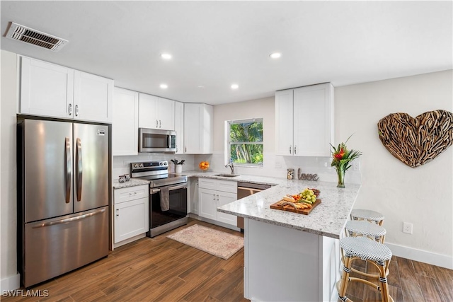 kitchen with appliances with stainless steel finishes, a kitchen bar, kitchen peninsula, and white cabinets