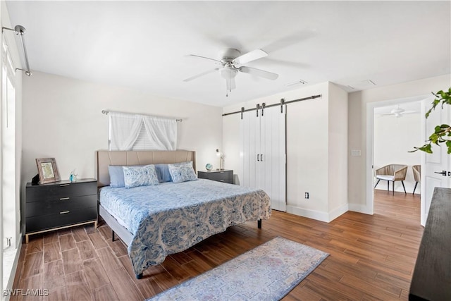 bedroom featuring dark hardwood / wood-style floors, a barn door, and ceiling fan