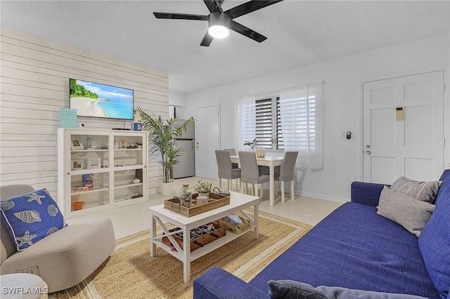 living room featuring a textured ceiling, wooden walls, ceiling fan, and light tile patterned flooring