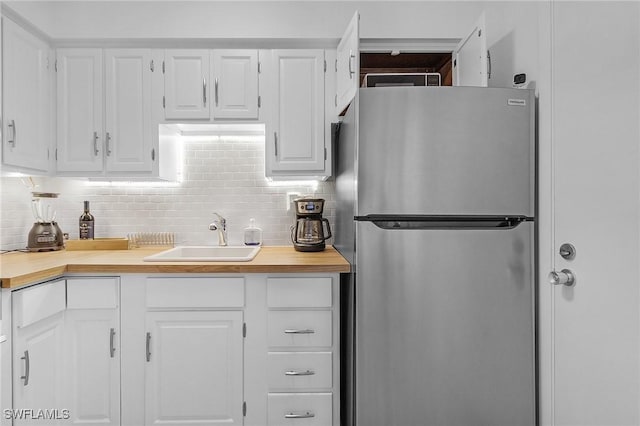 kitchen featuring stainless steel refrigerator, sink, decorative backsplash, and white cabinets