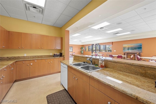 kitchen featuring dishwasher, sink, a drop ceiling, and light stone counters