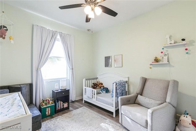 bedroom featuring dark hardwood / wood-style flooring, a nursery area, and ceiling fan