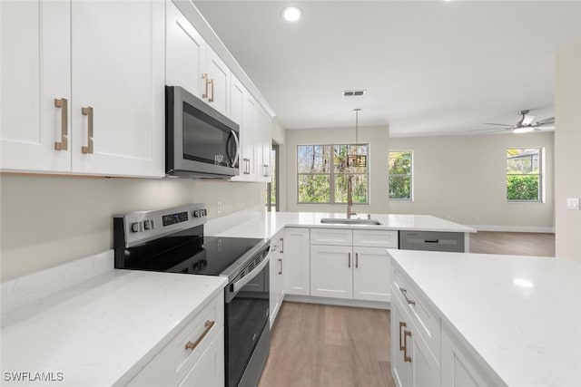 kitchen with light stone counters, hanging light fixtures, stainless steel appliances, and white cabinets