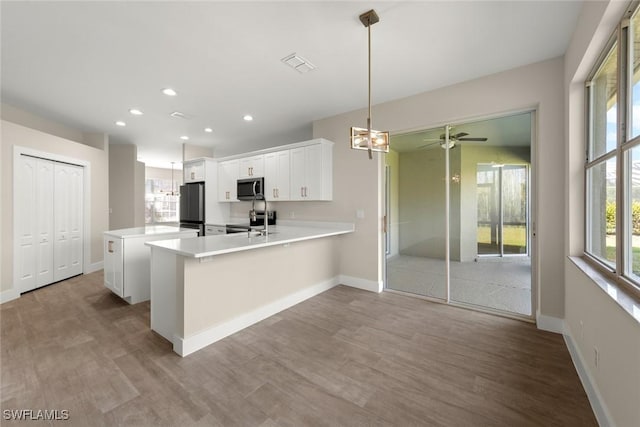 kitchen featuring appliances with stainless steel finishes, white cabinets, hanging light fixtures, light hardwood / wood-style floors, and kitchen peninsula