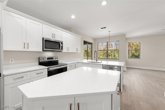 kitchen with sink, white cabinetry, decorative light fixtures, appliances with stainless steel finishes, and a kitchen island