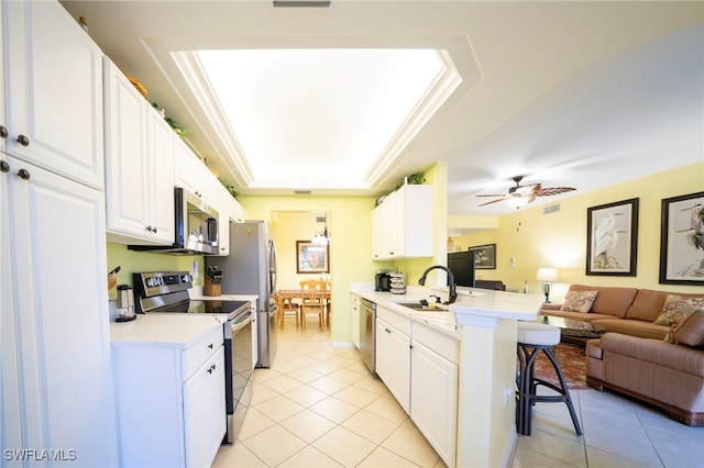 kitchen featuring a breakfast bar, sink, appliances with stainless steel finishes, a tray ceiling, and white cabinets